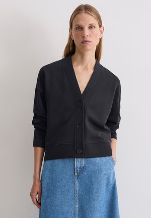 Czarny kardigan w serek z czterema guzikami, z prążkowanymi mankietami i dole, noszony na dżinsowej spódnicy. Gładka faktura, casualowy design.