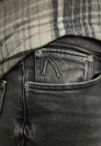 Gray denim jeans with a pocket design featuring a distinctive A-shaped embroidery. Metallic button accents on the waistband.