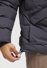 Chaqueta acolchada negra con un diseño voluminoso, tejido texturizado y un ajuste con presilla ajustable en el dobladillo para un ajuste personalizado.