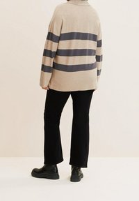 Beige stickad tröja med marinblå horisontella ränder, avslappnad passform och krage. Kombinerad med svarta vida byxor och svarta ankelstövlar.
