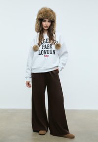 Šedá mikina s textem "REGENT'S PARK LONDON", hnědé široké kalhoty a čepice s kožešinovým podšívkou a bambulkami. Měkká textura, ležérní design.