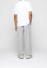 Pantalon gris clair à jambes larges associé à un t-shirt blanc uni. Tissu lisse avec une coupe décontractée. Des baskets casual complètent le look.