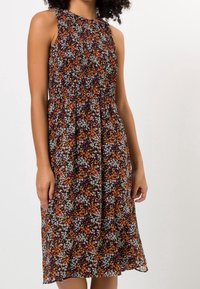 Robe midi sans manches avec une taille froncée, présentant un motif floral dense en orange, blanc et vert sur un fond foncé.