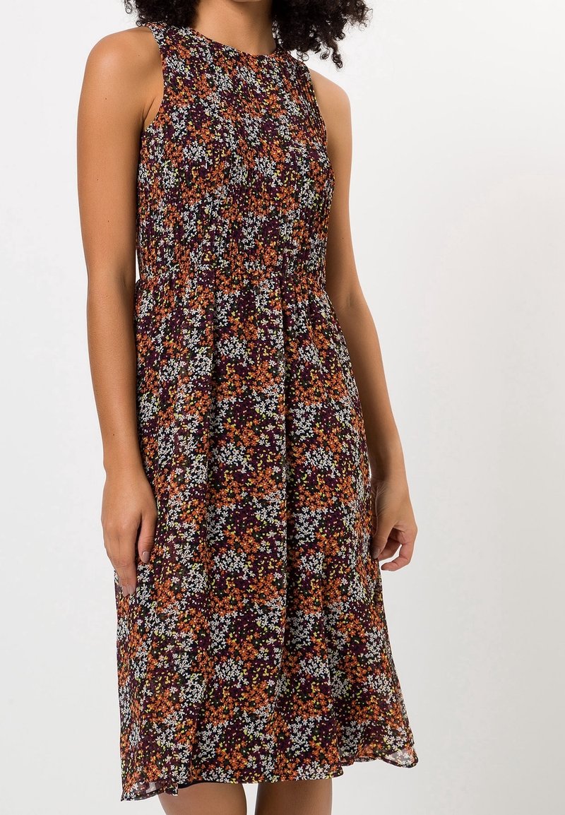 Robe midi sans manches avec une taille froncée, présentant un motif floral dense en orange, blanc et vert sur un fond foncé.