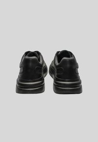 Chaussures de sport noires avec un dessus en cuir lisse, un col rembourré et une semelle extérieure en caoutchouc texturé et strié. La vue arrière met en avant un design minimaliste.