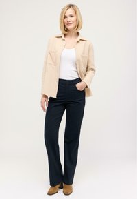 Beige wool blend shirt jacket with two front pockets, paired with navy trousers and brown suede ankle boots. White tank top underneath.