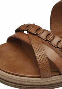 Hnědé kožené sandále s tkanými popruhy, texturovanými akcenty a plochou podrážkou. Důraz na neutrální tóny a hladké povrchy.