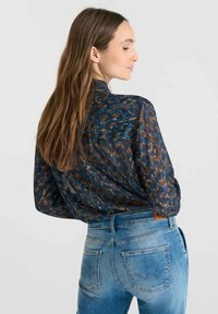 Brown and blue patterned blouse with a back yoke design, paired with light blue fitted jeans featuring a distinct back pocket design.
