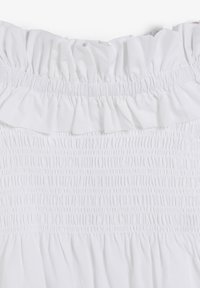 Top blanco con un cuerpo fruncido y cuello con volantes. La tela es ligera, con una textura suave y detalles fruncidos en todo su diseño.