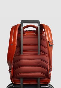 Rode leren rugzak met een gestructureerde, gepolsterde rug, voorzien van verstelbare banden en een uitschuifbare handgreep voor vervoer op wielen.