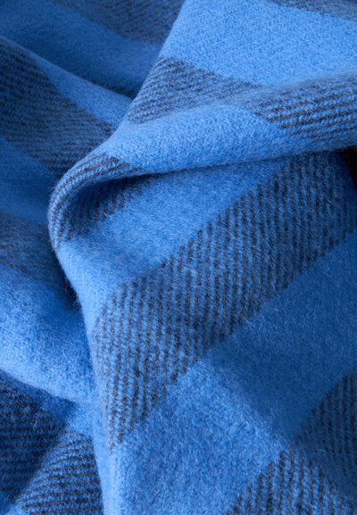 Tissu en laine à carreaux bleu doux et gris foncé, plié et superposé, montrant les détails de la texture et du motif.