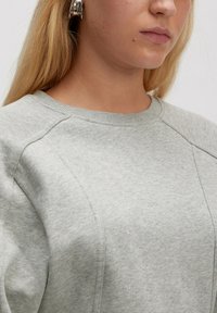 Sweatshirt gris clair avec col côtelé et coutures latérales. Texture douce, manches longues et coupe décontractée. Design minimaliste sans motifs.