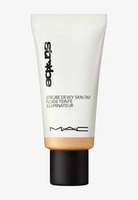 MAC Strobe Dewy Skin Tint dalam tabung squeeze putih dan emas dengan tutup hitam; memiliki desain ramping dan pelabelan jelas dalam cetakan gelap.