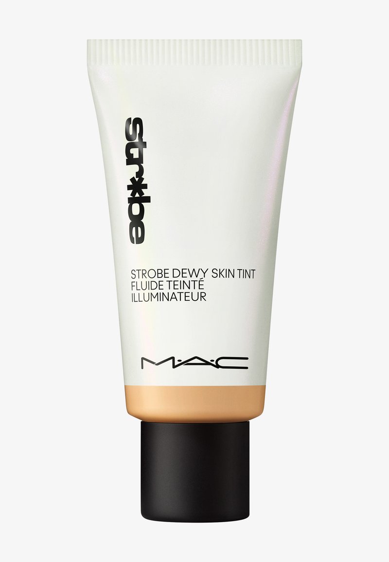 MAC Strobe Dewy Skin Tint dalam tabung squeeze putih dan emas dengan tutup hitam; memiliki desain ramping dan pelabelan jelas dalam cetakan gelap.