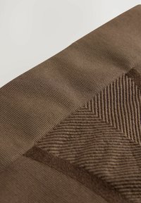 Bruine textiel met textuur, gekenmerkt door ribbel- en zigzagpatronen, met een gladde sectie aan de bovenkant en een ruwere textuur in het onderste deel.