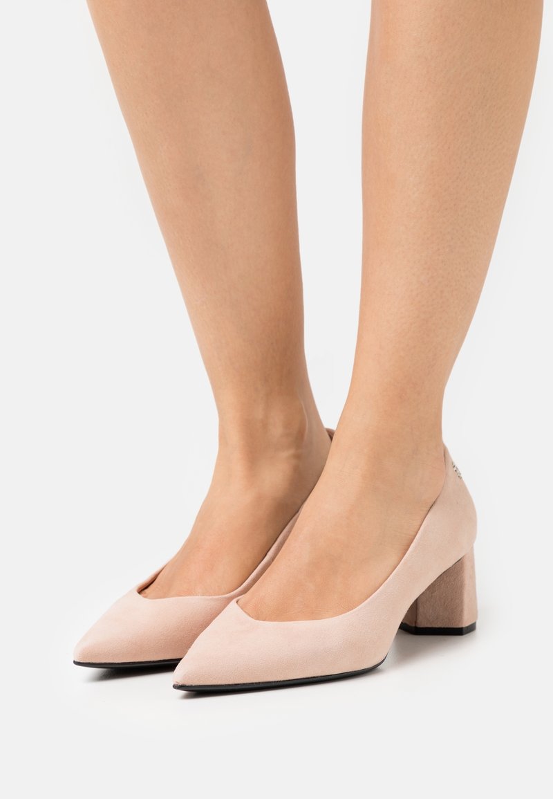 Escarpins en daim rose clair avec un bout pointu, une tige ouverte et un talon bloc texturé. Le design présente une finition lisse et une semelle noire contrastante.