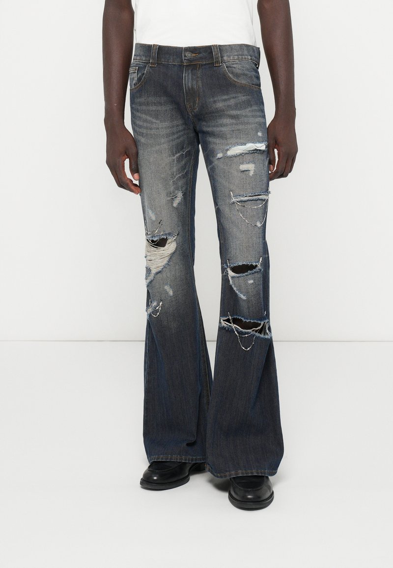 Δερμάτινα τζιν παντελόνια σε σκούρο μπλε χρώμα με φθορές και μεγάλες σκισμένες περιοχές; διαθέτει πέντε τσέπες και αντιπαραβαλλόμενο ραφές.