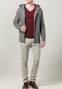 Szary dziergany kardigan z kapturem, wzór warkocza, zestawiony z bordowym swetrem z dekoltem w serek, jasnoszarymi dżinsami i brązowymi botkami do kostki.