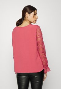 Top cor-de-rosa com mangas em renda, ajuste descontraído, decote redondo, apresenta detalhes em renda nas mangas, tecido suave e punhos ligeiramente alargados.