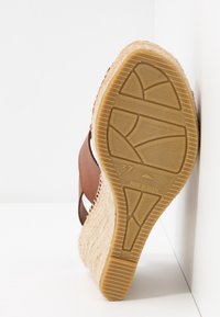 Sandale compensée avec talon en jute tressé et semelle en caoutchouc, taille 37, inclinée contre un mur et un sol blancs.