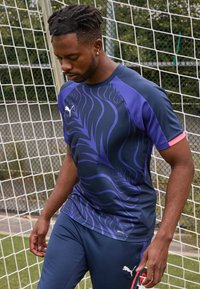 Mornarski športni kroj s dizajnom vijoličnih listov, kratkimi rokavi in rožnatimi poudarki, izdelan iz zračnega materiala. Kombiniran s spodnjimi hlačami v enaki barvi.