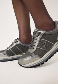 Graue Sneakers mit metallischen Akzenten, featuring ein Schnürdesign, strukturierte Paneele und eine dicke schwarze Laufsohle.