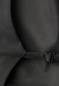 Primer plano de tela negra con una textura suave y un ligero brillo, acentuada por una pequeña hebilla rectangular negra y detalles de costura.