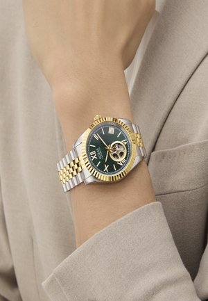 Two-tone wristwatch with a green dial, gold-accented bezel and Roman numerals, featuring a skeleton design and a silver and gold bracelet.