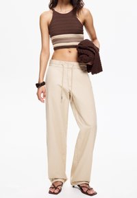 Brun og creme stribet strikket cropped top med halterneck, parret med beige vide bukser med snøre i taljen og sidelommer.
