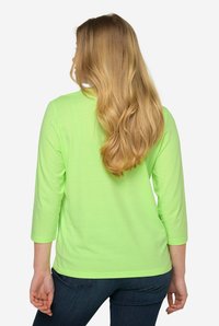 Langärmliges Shirt aus leuchtend neongrünem Stoff, mit rundem Ausschnitt und lockerer Passform. Die Rückansicht betont die glatte Textur und die Nähte.