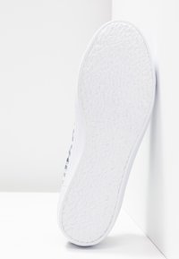 Biała podeszwa do sneakersów z teksturowaną gumą, posiadająca wzorzysty bok, gładkie krawędzie oraz zakrzywiony obcas. Zaprojektowana do noszenia na co dzień.