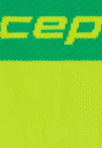 Close-up van groene en gele gebreide stof met gedeeltelijke gele tekst op groene achtergrond.