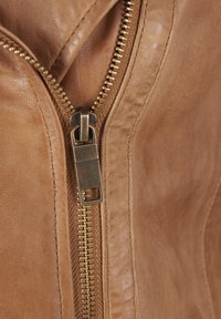 Tessuto in pelle marrone con una zip visibile; hardware della zip in ottone con un robusto tirante quadrato; texture liscia con alcune venature naturali.