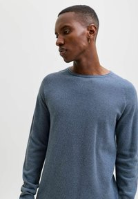 Blå strikket genser med strukturert mønster, rund hals, og lange ermer, med en tettsittende passform uten logoer.