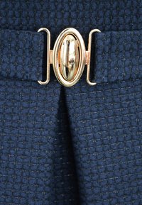 Granatowy, teksturowany materiał w diamentowy wzór, z akcentem w postaci złotego owalnego zapięcia. Materiał jest tkany z delikatnym połyskiem.