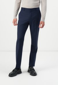 Pantalones ajustados azul marino, cortados a medida, hechos de una tela suave. Combinados con un suéter ligero y mocasines negros.