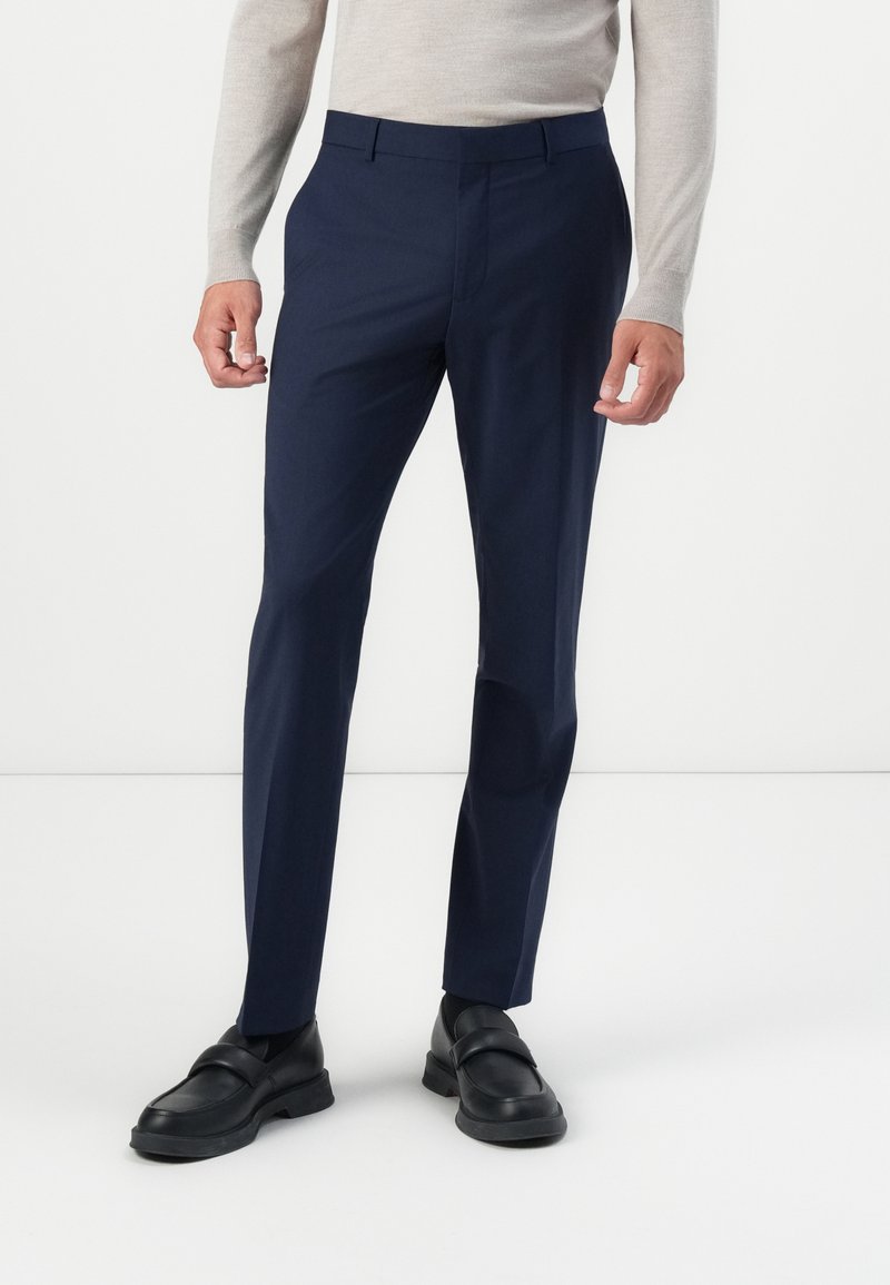Pantalones ajustados azul marino, cortados a medida, hechos de una tela suave. Combinados con un suéter ligero y mocasines negros.