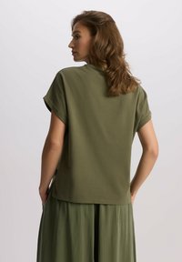 Oliwkowa koszula z krótkim rękawem, wykonana z lekkiego materiału, o luźnym kroju i podsuniętych rękawach. W zestawie ze dopasowaną plisowaną spódnicą.