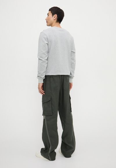 Gray sweatshirt and dark green cargo pants. Pants feature side zippers and multiple pockets. Smooth fabric texture, relaxed fit.