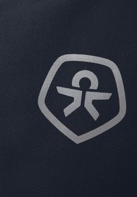Ciemnoniebieska tkanina z srebrnym emblematem w kształcie tarczy i abstrakcyjną figurą ludzką, prezentująca teksturowaną powierzchnię.