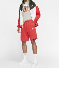 Červené šortky Nike s elastickým pasem a šňůrkou. Šedé tričko s potiskem pod barevnou bundou s černými, bílými a žlutými panely. Bílé tenisky.