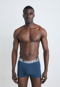 Donkerblauwe boxershorts met een witte, gebrandmerkte tailleband, gladde textuur en slim-fit ontwerp, gedragen door een shirtloze mannelijke modellen.