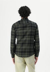 Camisa de cuadros negra y verde con mangas largas, puños con botones, dobladillo redondeado y un cuello. Fabricada con una tela suave con una apariencia texturizada.