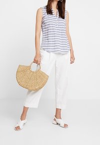 Blusa sin mangas a rayas en azul y blanco, combinada con pantalones blancos recortados y un bolso redondo de paja tejido. El calzado consiste en sandalias blancas con tiras cruzadas.