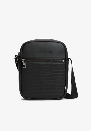 Bolso bandolera negro de Tommy Hilfiger con bolsillo frontal con cremallera, textura tejida, logo en relieve y correa de hombro ajustable.