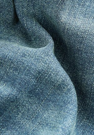 Blauwe denimstof met een gestructureerd weefsel, met verschillende tinten blauw en subtiele vervaging, die de zachtheid en flexibiliteit ervan benadrukt.