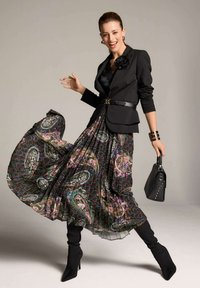 Zwarte blazer met een stoffen bloem, gelaagde geplooide rok in donkere tinten met paisleypatronen, zwarte stiletto laarzen en een kleine zwarte handtas.