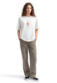 Witte katoenen t-shirt met korte mouwen, voorzien van een oranje en roze grafische print in het midden, gecombineerd met losse, olijfgroene broeken.