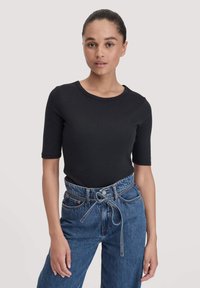 Zwarte korte mouwen top met een ronde halslijn, gecombineerd met hoge blauwe spijkerbroek met een strikceintuur en een knoopsluiting aan de voorkant.