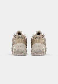 Sapatilhas bege com um cabedal liso em camurça e malha, apresentando o logo "aim" e o swoosh da Nike, sola texturizada com padrões em onda, projetadas para conforto.
